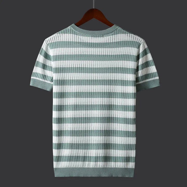 A short-sleeve, light green and white horizontal striped knit shirt with a comfort-fit design is displayed on a brown wooden hanger against a dark gray background. The back of the shirt is visible.
