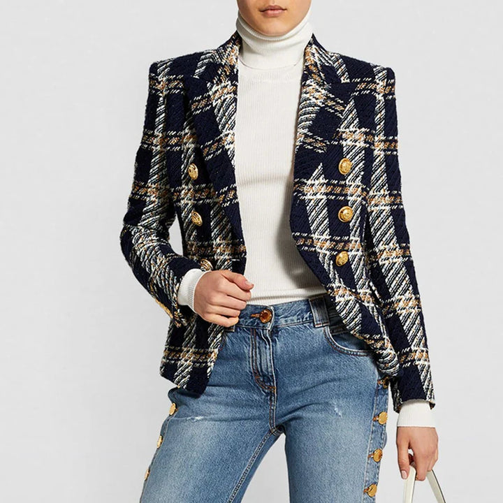 A person wearing a slim fit navy blue plaid wool tweed blazer with gold buttons over a white turtleneck sweater and blue jeans with button details, holding a white bag. The head is partially out of frame.