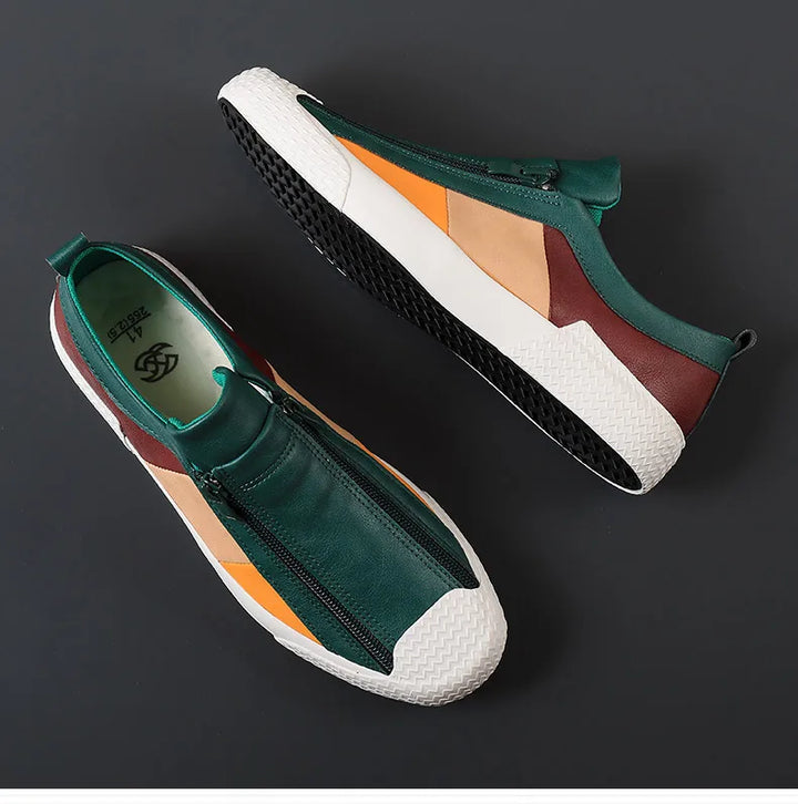A pair of stylish sneakers with green, brown, orange, and beige panels, white textured soles, and black treads are displayed on a dark background. The shoes feature a front zipper closure and a cushioned sole for extra comfort.
