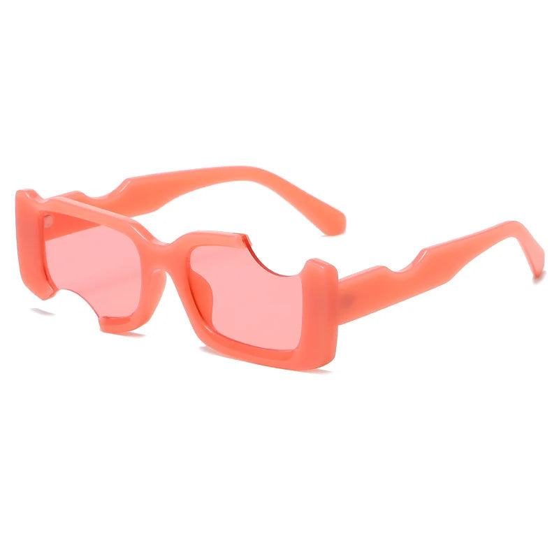 Rectangular avant-garde sunglasses featuring thick, coral pink frames and matching pink lenses. The jagged cut-out details on the top and sides create a bold, modern style perfect for those who love irregular sunglasses.