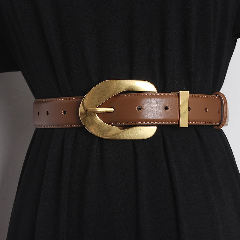 A person wearing a black outfit with a wide genuine leather belt at the waist, featuring an oversized buckle in shiny gold.