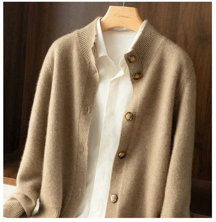 A beige, ultra soft cashmere cardigan with buttons is displayed on a hanger over a white collared shirt, set against a wooden background.
