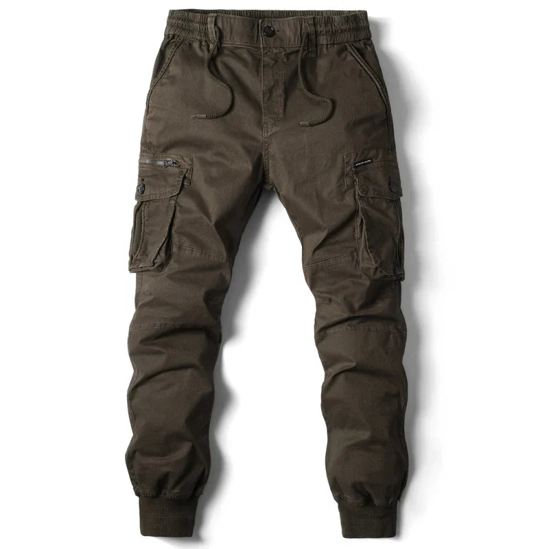 Dark brown street style cargo jogger pants with an elastic waistband, drawstring, side and flap cargo pockets, button and zipper closure, and elastic cuffs at the ankles. Pants are laid flat on a white background.