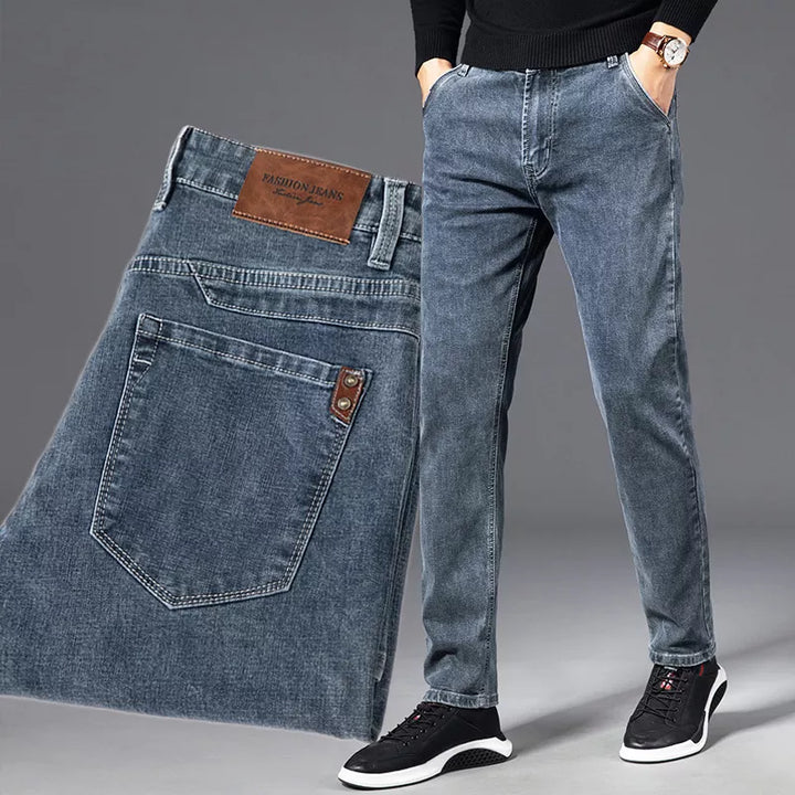 A person wearing straight-leg jeans with hands in pockets, paired with a black shirt and black sneakers. An enlarged view of the durable denim back pocket and leather label is shown to the left. The background is plain gray.