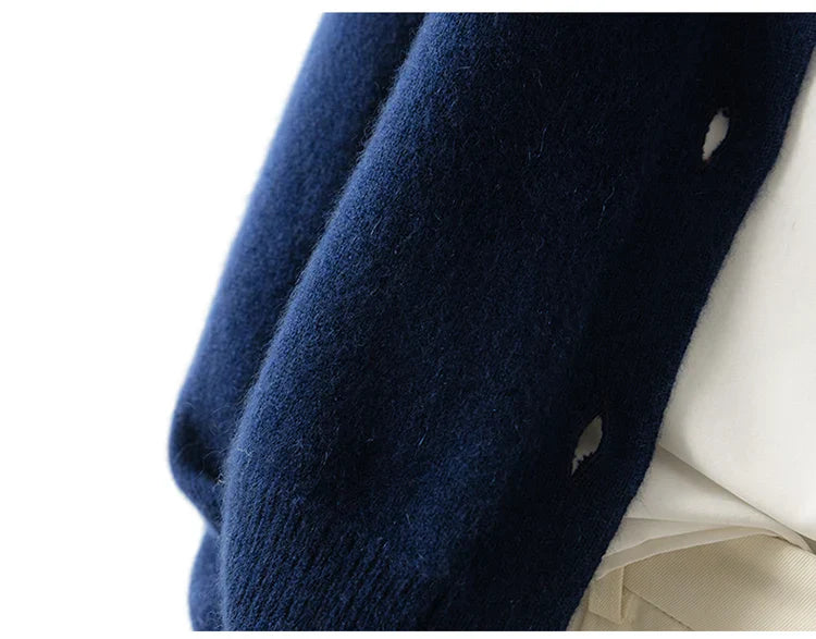 Close-up of a person wearing an ultra soft, dark blue cashmere cardigan draped over a light-colored shirt, showing buttonholes along the edge of the sweater.