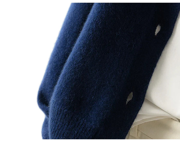 Close-up of a person wearing an ultra soft, dark blue cashmere cardigan draped over a light-colored shirt, showing buttonholes along the edge of the sweater.