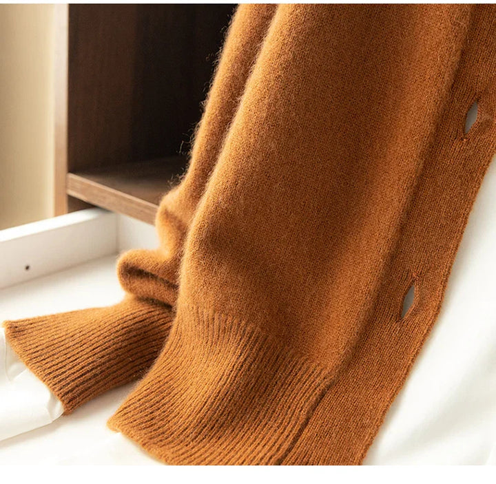 A close-up of an ultra soft, brown cashmere cardigan draped over a white surface, with ribbed cuffs and hem visible, and a wooden background partially in view.