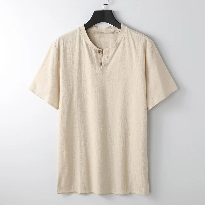 A beige short-sleeve shirt crafted from lightweight breathable Japanese linen, featuring a round neckline and two buttons, hangs on a black hanger against a plain white background.