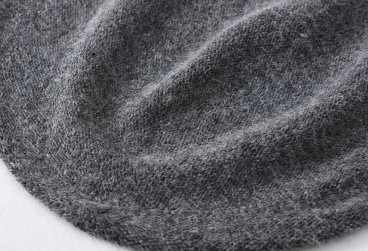 A close-up of a soft, grey cashmere wool fabric with visible texture and gentle folds, suggesting the warmth and comfort of a lightweight, slouchy beanie.