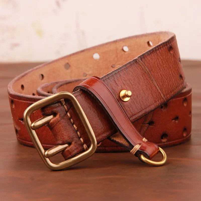 A vintage leather belt with a brass buckle, coiled on a wooden surface. Crafted from premium leather, it features multiple holes along its length and a small gold stud near the end.