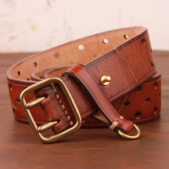 A vintage leather belt with a brass buckle, coiled on a wooden surface. Crafted from premium leather, it features multiple holes along its length and a small gold stud near the end.