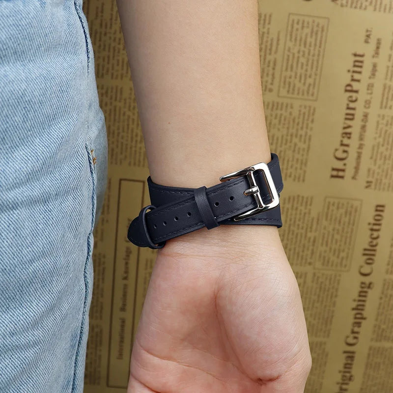 A person wearing light blue jeans and a black genuine leather Apple Watch band with a silver buckle on their wrist, shown against a tan background with text printed on it.