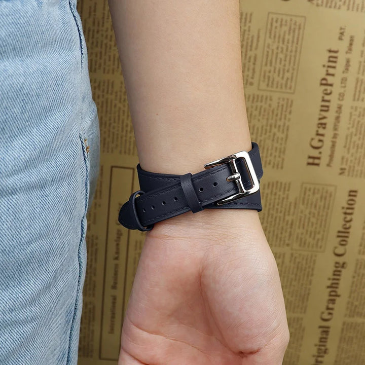 A person wearing light blue jeans and a black genuine leather Apple Watch band with a silver buckle on their wrist, shown against a tan background with text printed on it.