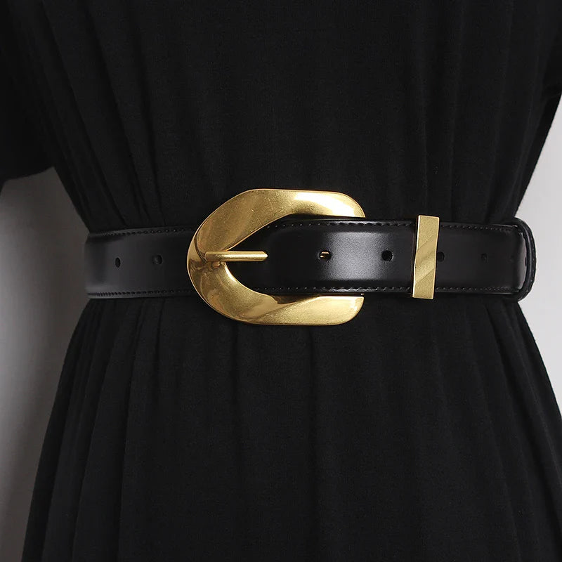 A black dress is cinched at the waist with an adjustable belt featuring a large, shiny, gold oval buckle and gold details.