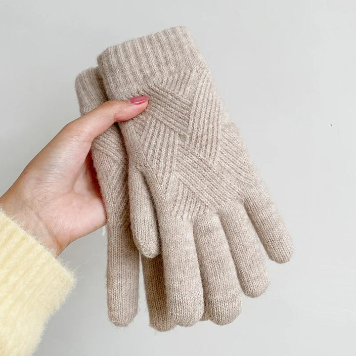 A hand holds a pair of luxurious beige knitted gloves with a subtle textured pattern, made from a soft cashmere blend, shown against a plain light background.