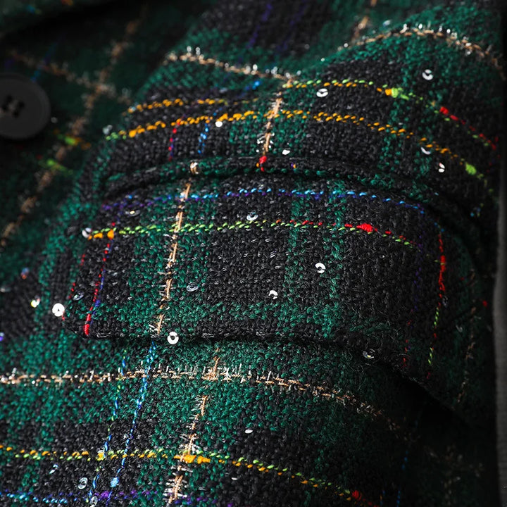 Close-up of a textured green and black tweed fabric with a plaid pattern, colorful threads, small sequins, and a black button—perfect details for a stylish jacket coat or formal blazers, showing part of a jacket pocket or sleeve.