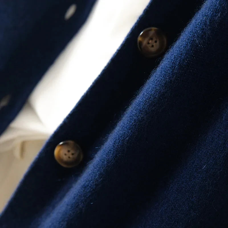 Close-up of a navy blue 100% wool cashmere coat featuring brown buttons, with a glimpse of a white shirt underneath. The fabric appears ultra soft and textured.