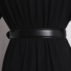 A close-up of a genuine leather belt with an oversized buckle cinched around the waist of a person wearing a black garment, shown from the back.