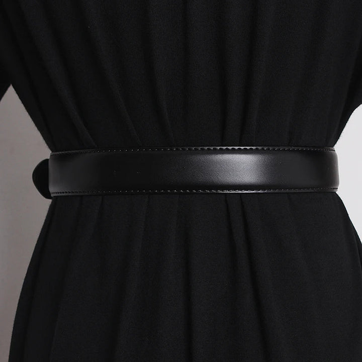 A close-up of a genuine leather belt with an oversized buckle cinched around the waist of a person wearing a black garment, shown from the back.