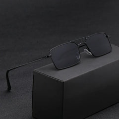 A pair of black rectangular sunglasses with thin, lightweight alloy frames rests on a black box, set against a dark, textured background.