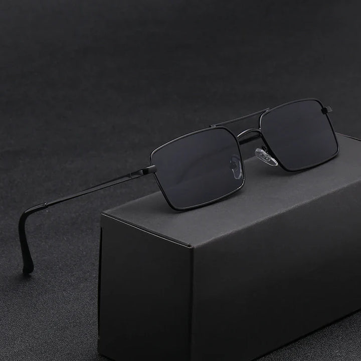 A pair of black rectangular sunglasses with thin, lightweight alloy frames rests on a black box, set against a dark, textured background.
