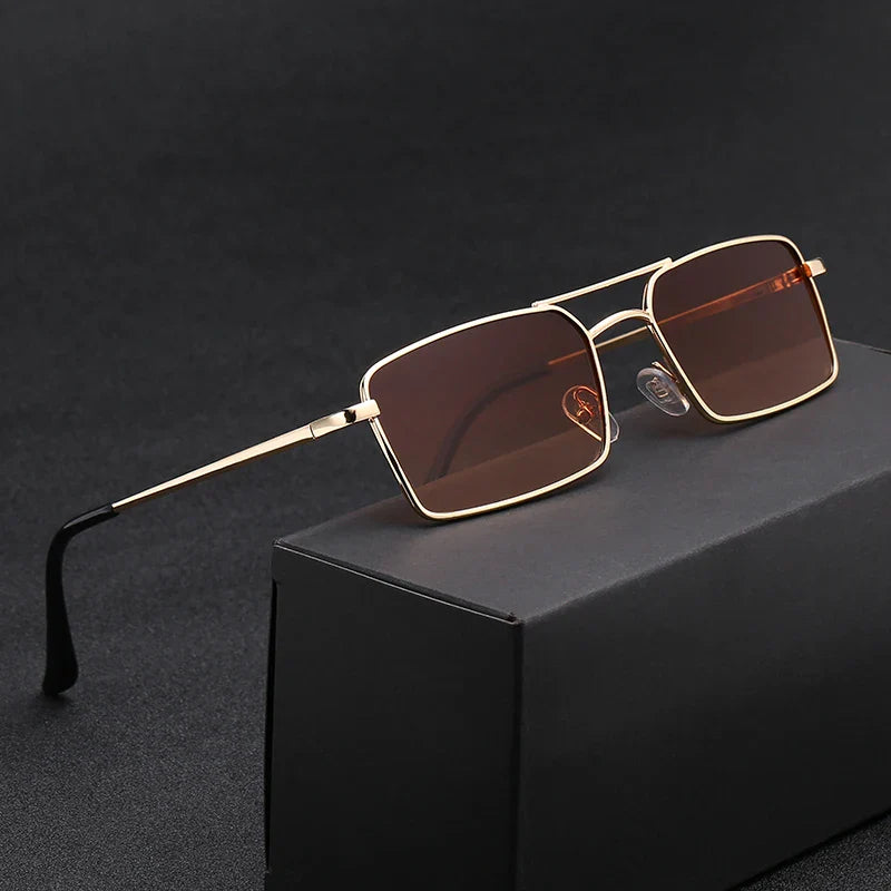 A pair of rectangular sunglasses with gold lightweight alloy frames and dark brown lenses, offering UV400 protection, displayed resting on a black box against a dark background.