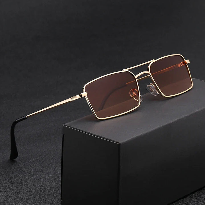 A pair of rectangular sunglasses with gold lightweight alloy frames and dark brown lenses, offering UV400 protection, displayed resting on a black box against a dark background.
