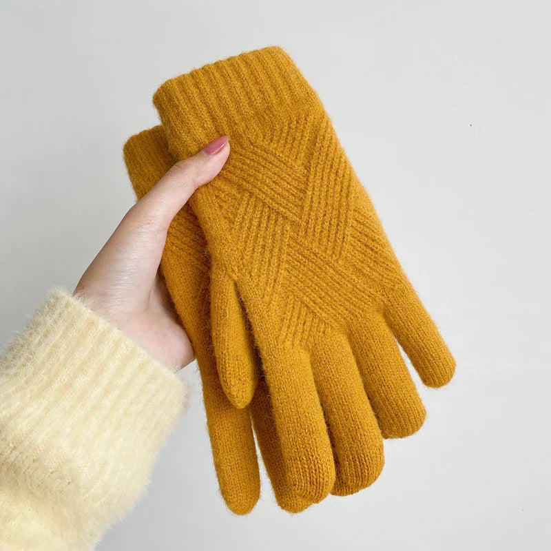 A person wearing a light cream sweater holds a pair of luxurious, mustard yellow knitted gloves made from a soft cashmere blend against a plain white background.