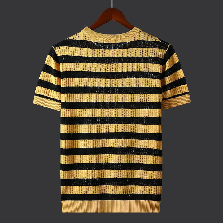 A short-sleeve knit shirt with horizontal yellow and black stripes, crafted from a silk cotton blend, displayed on a wooden hanger against a dark background. The shirt features a ribbed neckline, sleeves, and hem.
