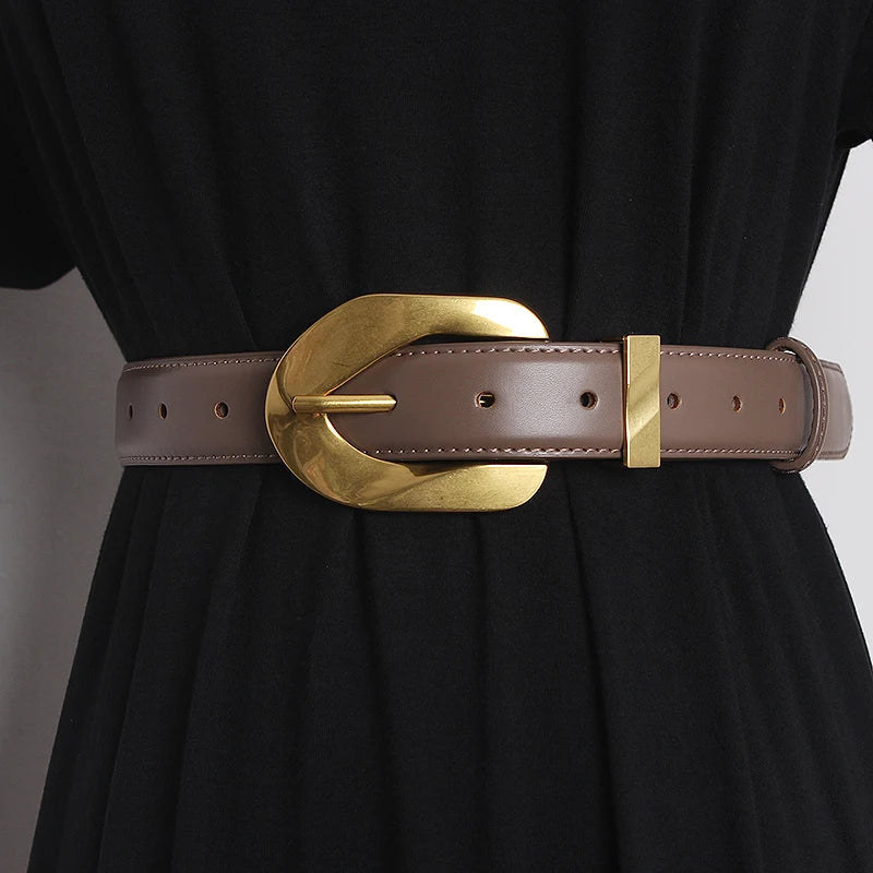 A close-up of a genuine leather belt with an oversized, shiny gold buckle, worn around a black dress.