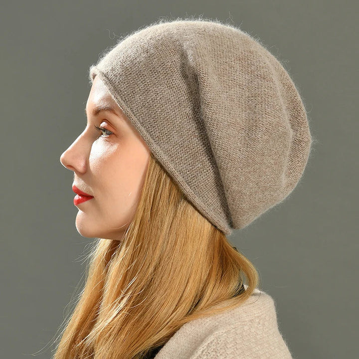 A woman with long blonde hair, wearing a light brown slouchy beanie, is shown in profile against a plain gray background.