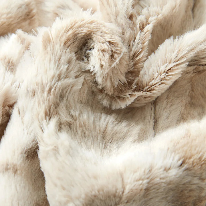 Close-up of ultra-soft luxurious blanket in beige faux fur, showcasing its plush, fluffy texture and subtle color variations, with wavy folds and gentle shadows.