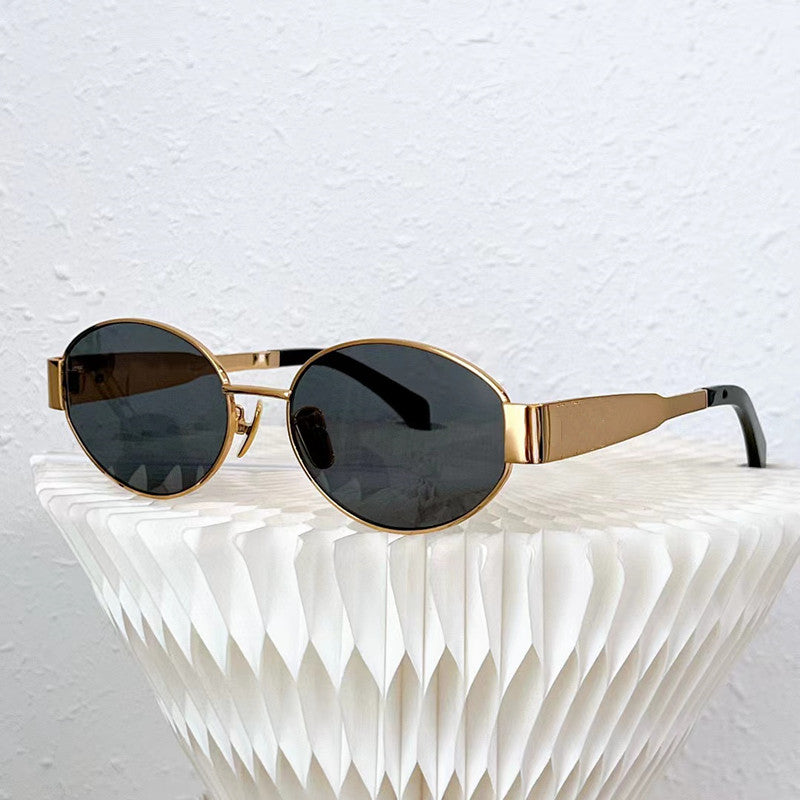 Vintage-inspired sunglasses with gold oval frames and dark UV400 protection lenses rest on a white, textured, geometric surface against a light-colored wall.