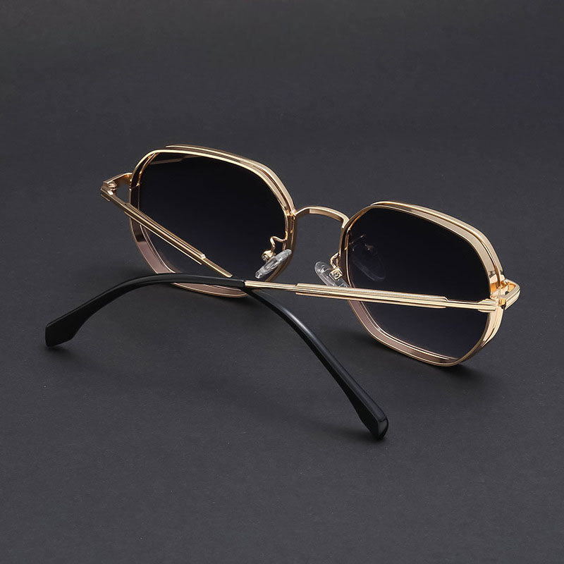Vintage-inspired sunglasses featuring gold-tone frames with UV400 protection, dark gradient lenses, and black temple arms rest on a dark surface, viewed from an angle behind the glasses.