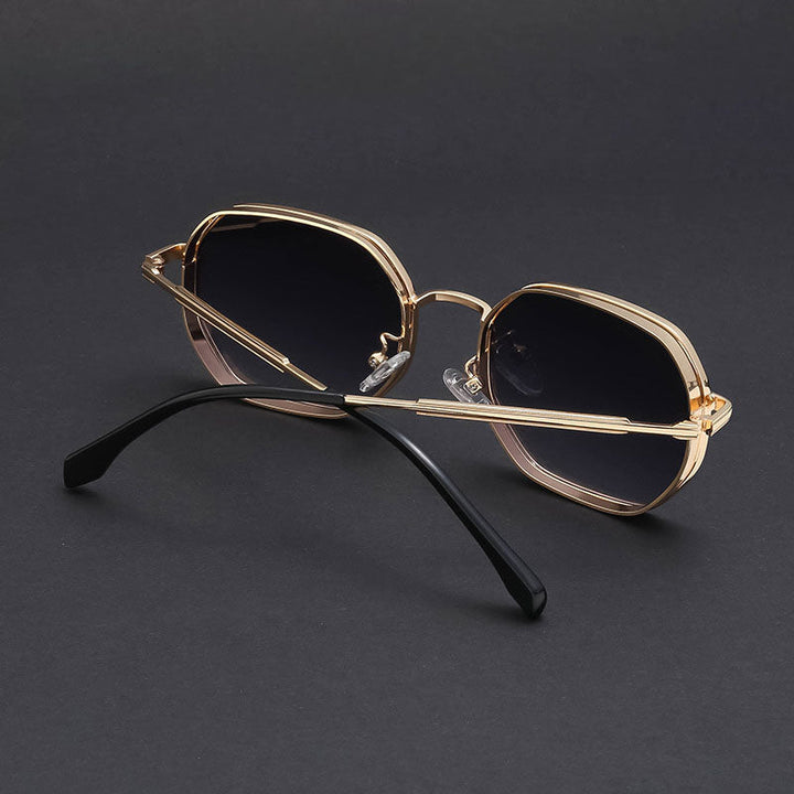 Vintage-inspired sunglasses featuring gold-tone frames with UV400 protection, dark gradient lenses, and black temple arms rest on a dark surface, viewed from an angle behind the glasses.