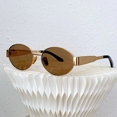 Gold-framed oval sunglasses with brown lenses rest on a white, textured, geometric surface against a plain white wall background, exuding Italian style and effortless sophistication.