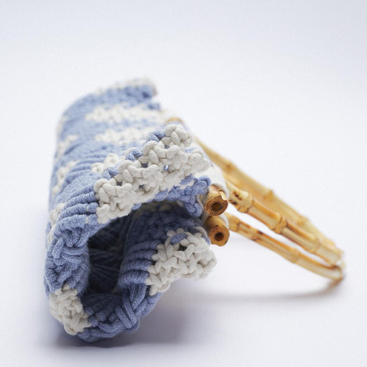A close-up of a lightweight bag with blue and white knitted fabric and bamboo handles, set against a plain white background.