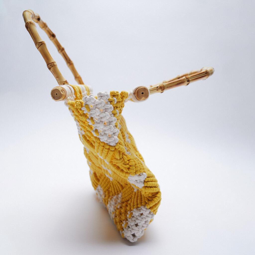 A yellow and white crocheted macramé handbag with a textured pattern and two curved bamboo handles, displayed against a plain white background.