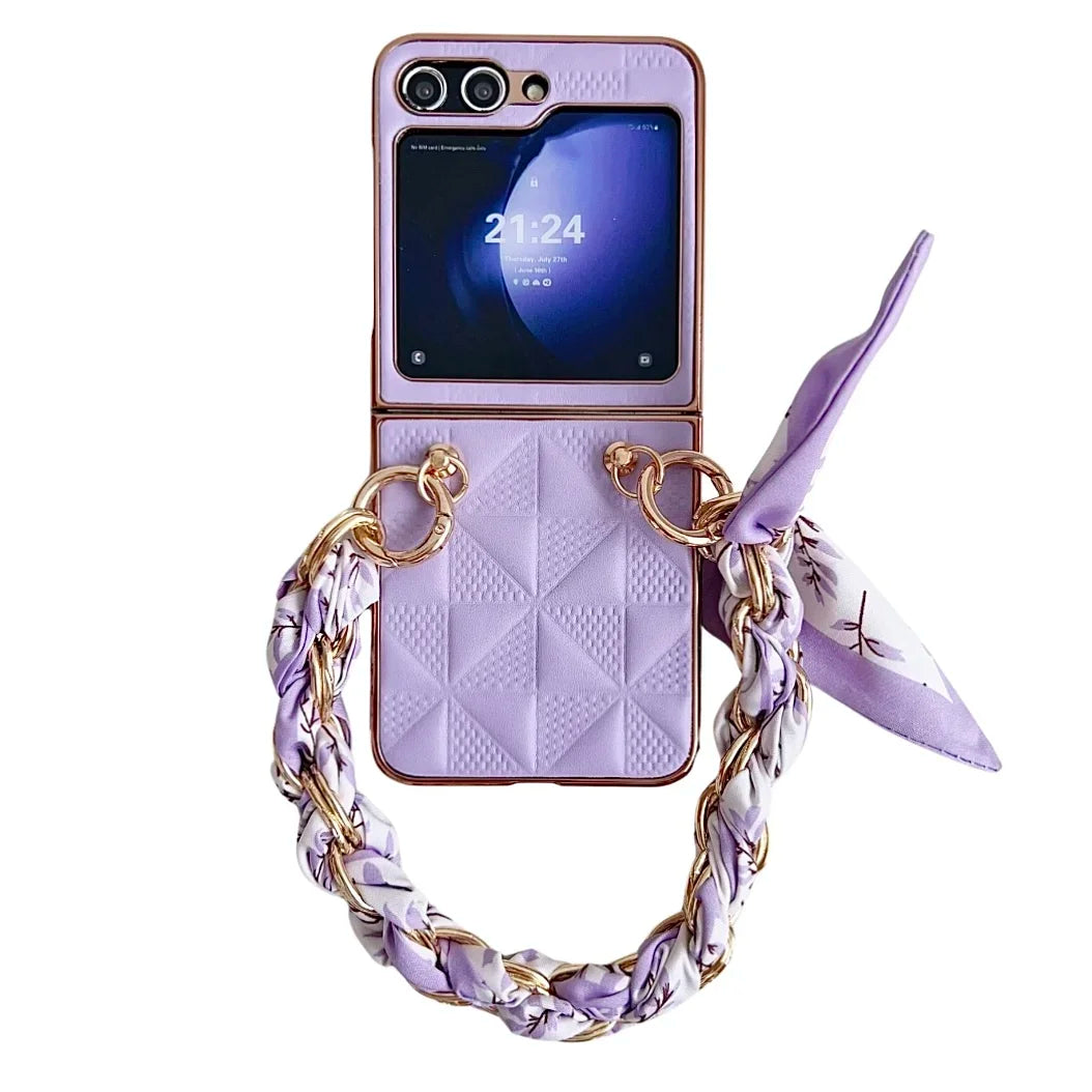 A lavender Samsung Galaxy Z Flip phone case with a geometric pattern, gold rings, a braided chain handle woven with a matching scarf, a small external screen displaying 21:24, and shockproof protection.