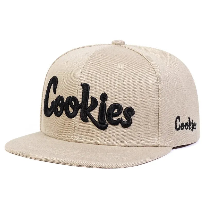 A beige flat-brimmed baseball cap with Cookies embroidered in large black script on the front and smaller Cookies text on the side, crafted from breathable fabric for comfort. Features an adjustable strap for a perfect fit.