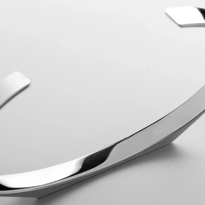 Close-up of a minimalist wall clock with a smooth, 18K gold plating metallic rim and raised hour markers on a light grey background. The design is clean and modern.