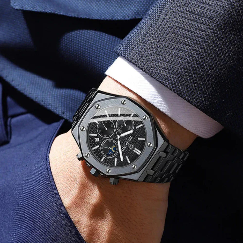 A person wearing a dark blue suit and white shirt displays a stylish black stainless steel watch with chronograph dials, a textured face, and metallic screws on the bezel.