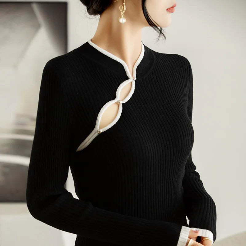 A woman wearing a black ribbed knit long-sleeve dress with two keyhole designs near the neckline, outlined in white trim and fastened with pearl-like buttons. She has pearl drop earrings and her hair is styled up.