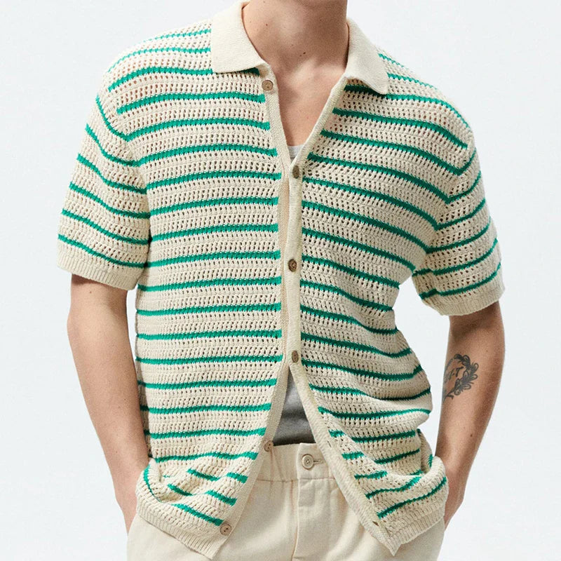 A person wearing a retro knit polo with an open-knit design, featuring green and beige stripes, cream pants, and a tattoo on their left forearm. Their head is not visible, giving the look a fresh streetwear edge.