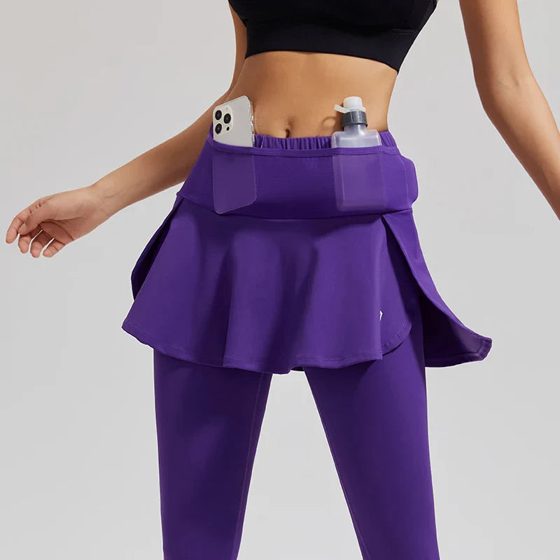 A woman wears high-waisted skirted leggings paired with a black sports bra; the purple sports skirt features stretch storage pockets, holding a smartphone and a bottle.