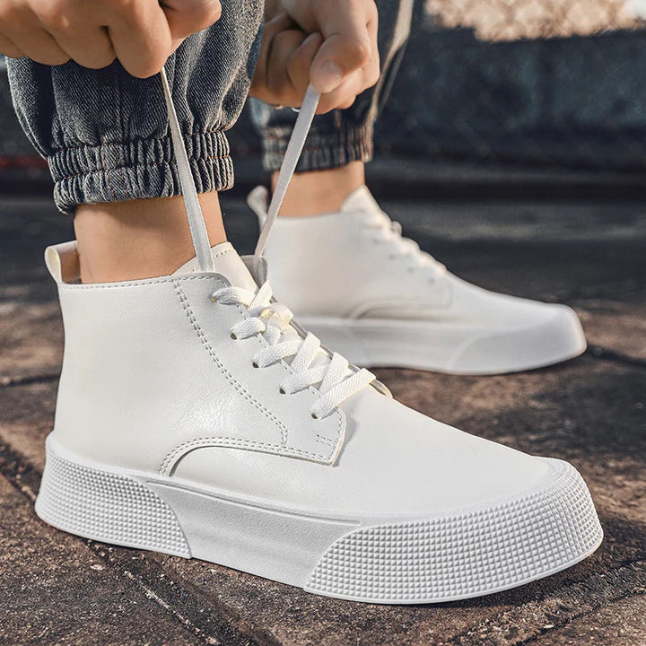 A person in cuffed jeans ties the laces of a vintage-inspired high-top white sneaker with a cushioned footbed while kneeling outdoors on pavement. Another matching sneaker rests in the background.