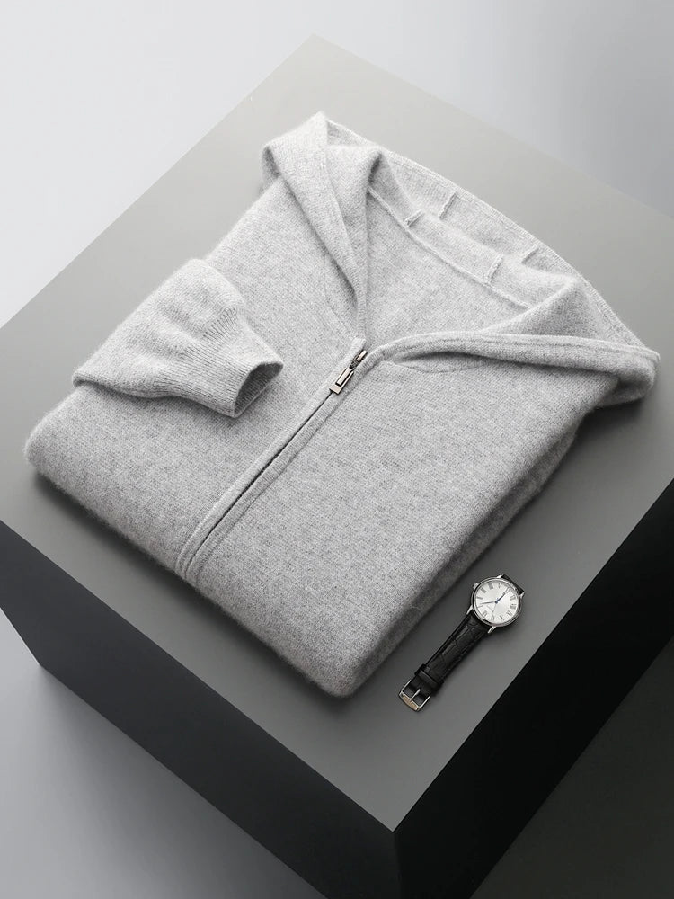 A light gray men wool cardigan zip-up sweater is neatly folded on a gray surface, with a black leather strap wristwatch placed beside it. The background has a minimalistic, modern appearance.