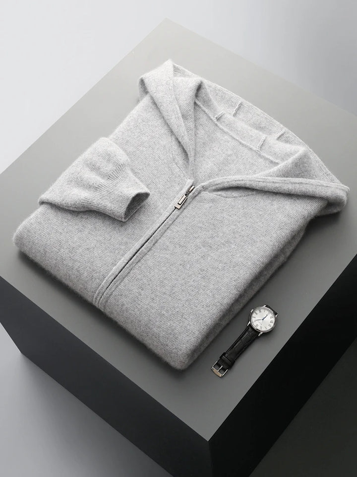 A light gray men wool cardigan zip-up sweater is neatly folded on a gray surface, with a black leather strap wristwatch placed beside it. The background has a minimalistic, modern appearance.