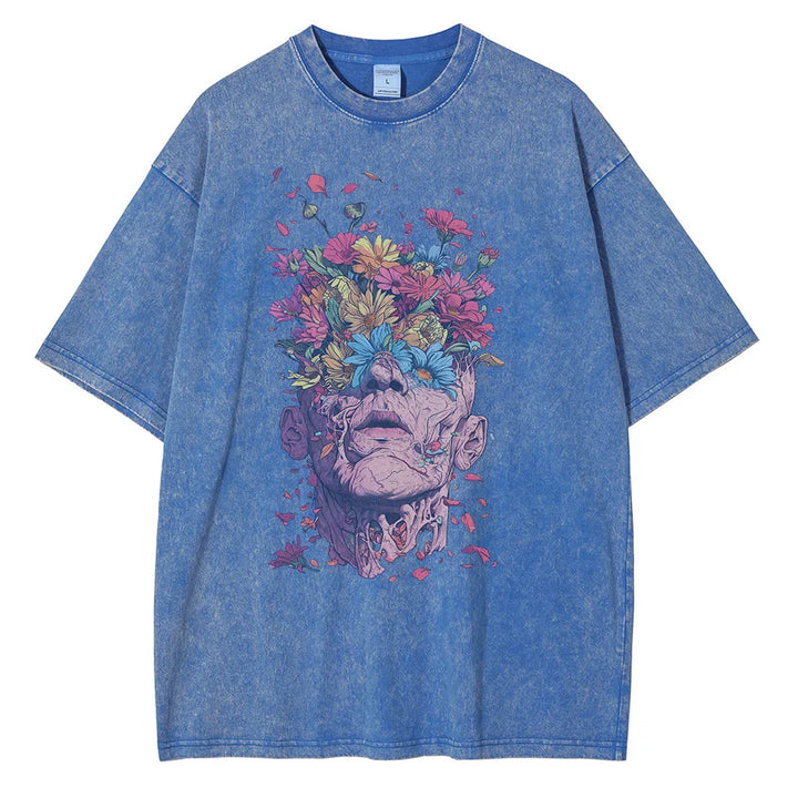 Blue denim-effect T-shirt in an oversized fit, featuring a premium cotton fabric and a graphic design of a human face with vivid flowers and foliage emerging from the head, blending surreal art and nature in pink, yellow, red, and blue tones.