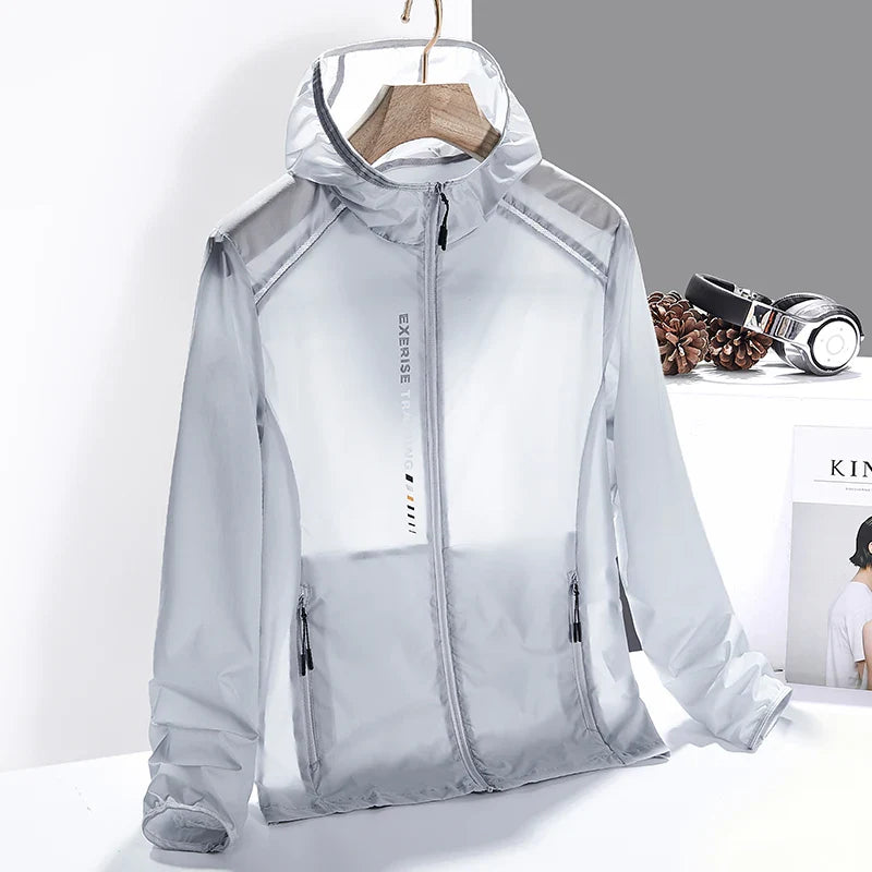 A light grey, semi-transparent hooded windbreaker jacket made of lightweight, quick-dry material is displayed on a wooden hanger. The jacket has black zipper pockets and EXERSE printed vertically on the front. Headphones and pinecones are in the background.